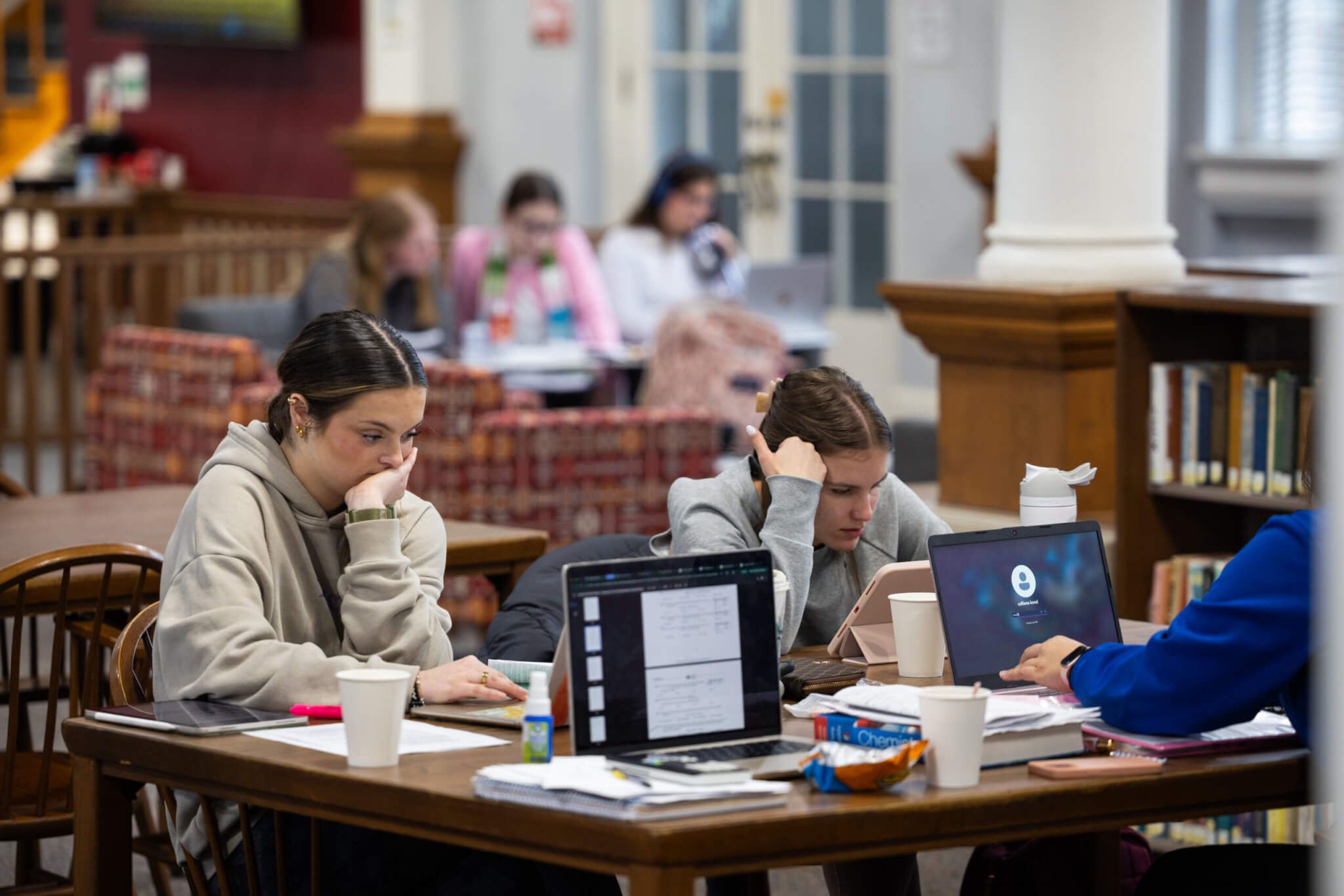 A group of students sitting around a table focusing on laptops and notebooks.