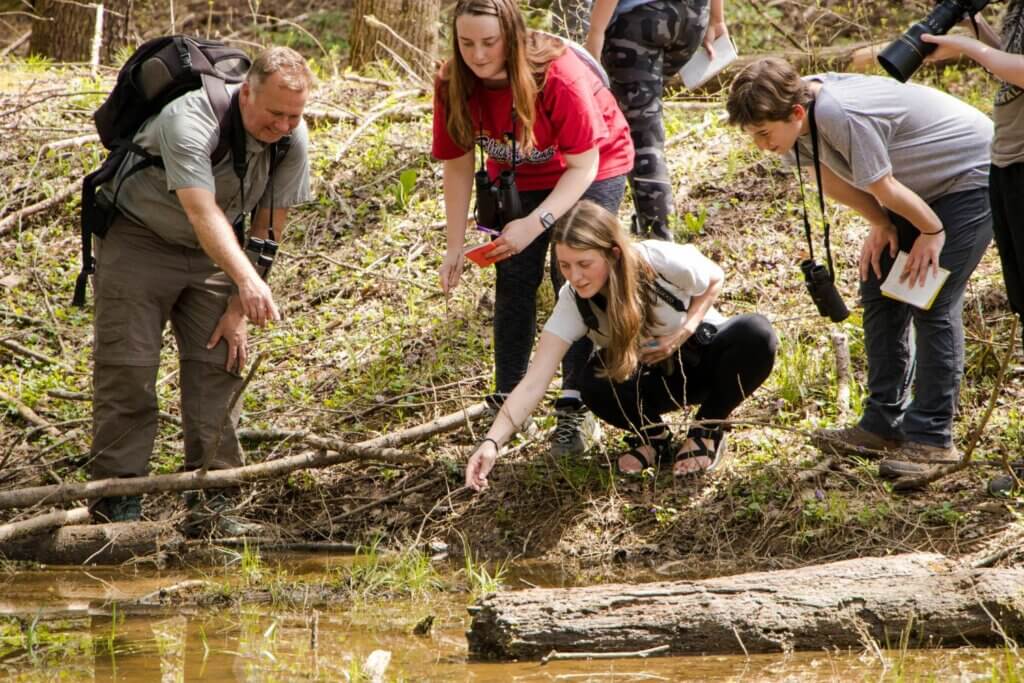 Photo of Maryville College students in the Great Smoky Mountains, examining water life while Dr. Drew Crain looks on