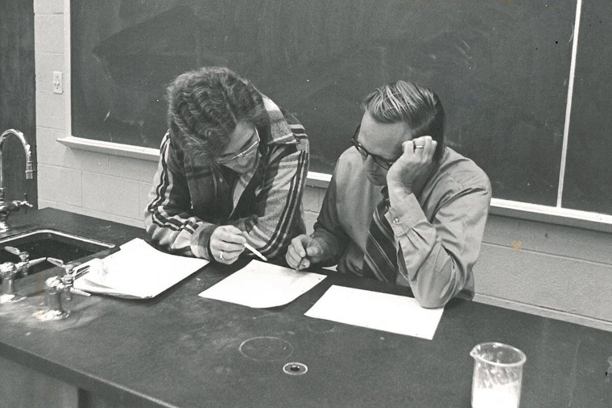 Black and white photo of Dr. William Dent going over paperwork with a student