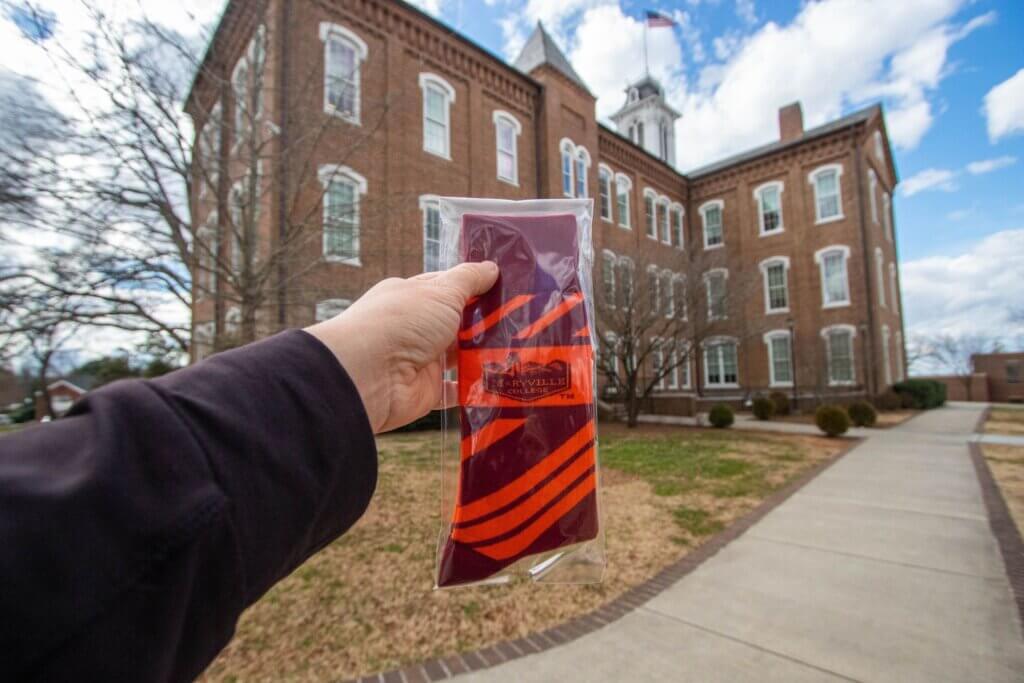 Photo of a hand holding a pair of tartan socks with Anderson Hall in the background