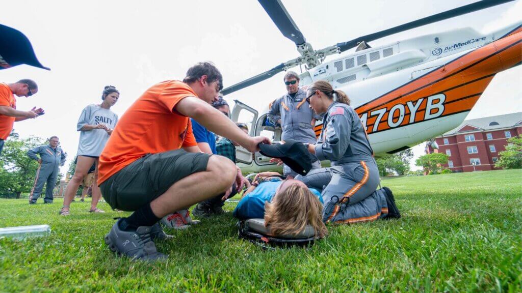 Photo of students participating in a mock wilderness rescue on Lloyd Beach, with the LIFESTAR medical helicopter in the background