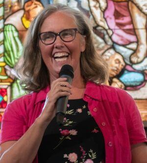 Photo of interim campus minister Jamie Webster with microphone in front of stained glass window