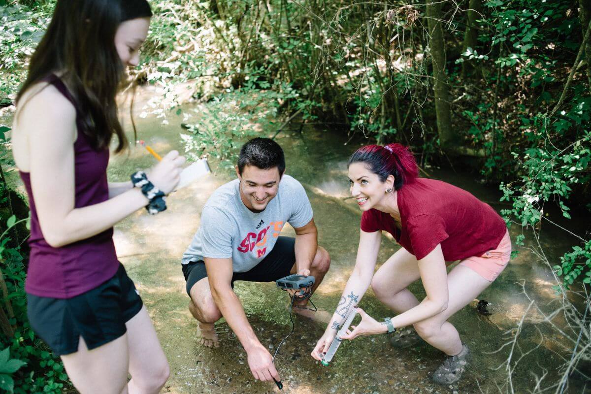 Photo of Dr. Joy Buongiorno and two students standing in a creek.