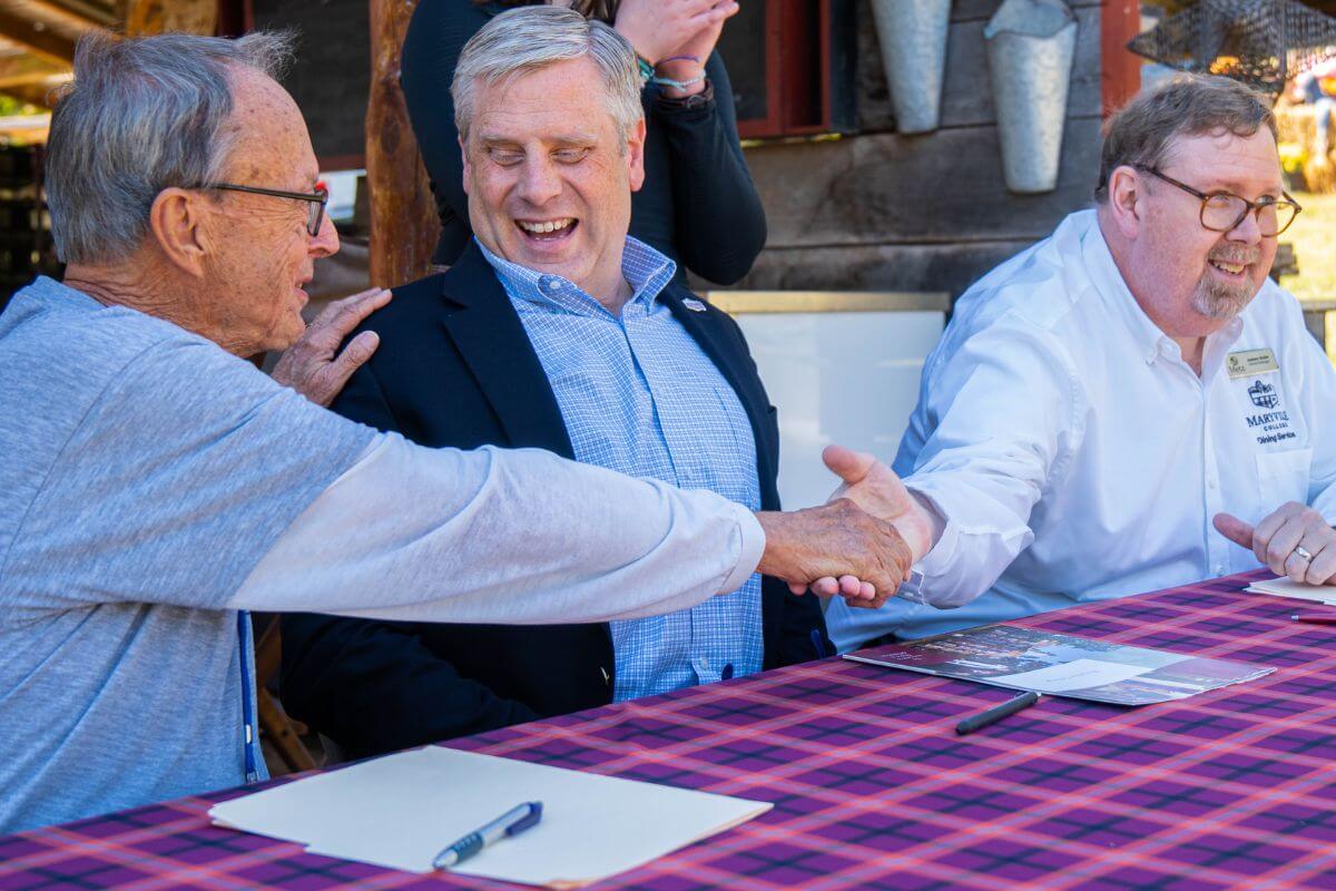 Photo of three men at a table laughing and shaking hands