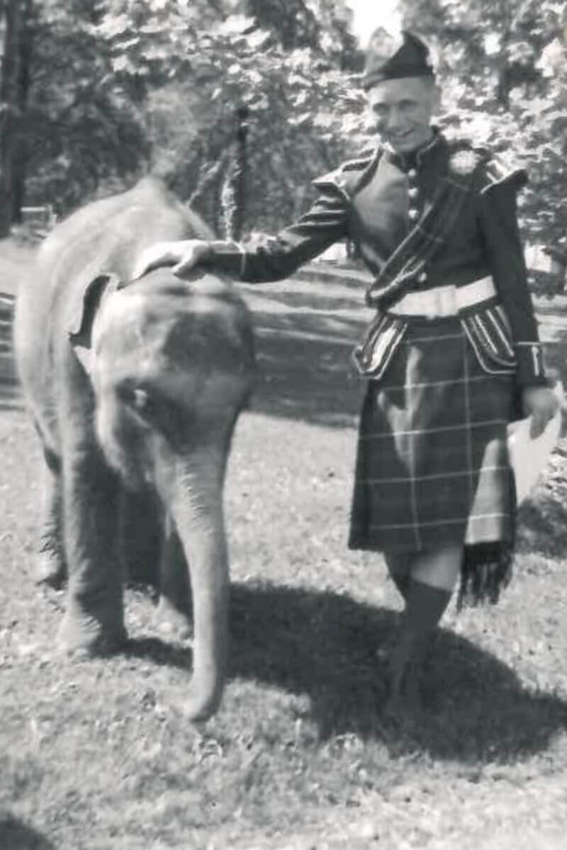 Black and white photo of an MC marching band student with a baby elephant