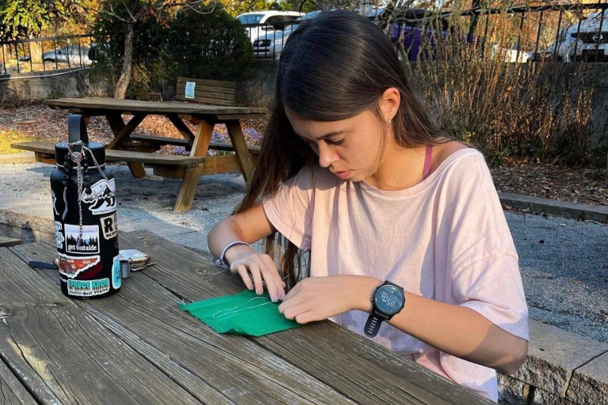 Photo of a student sewing fabric at a picnic table