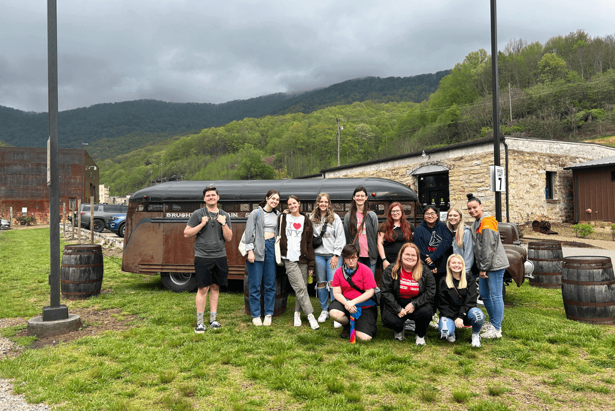 Dr. Rachel Ponder and eleven MC students stand in front of a old bus at Brushy Mountain