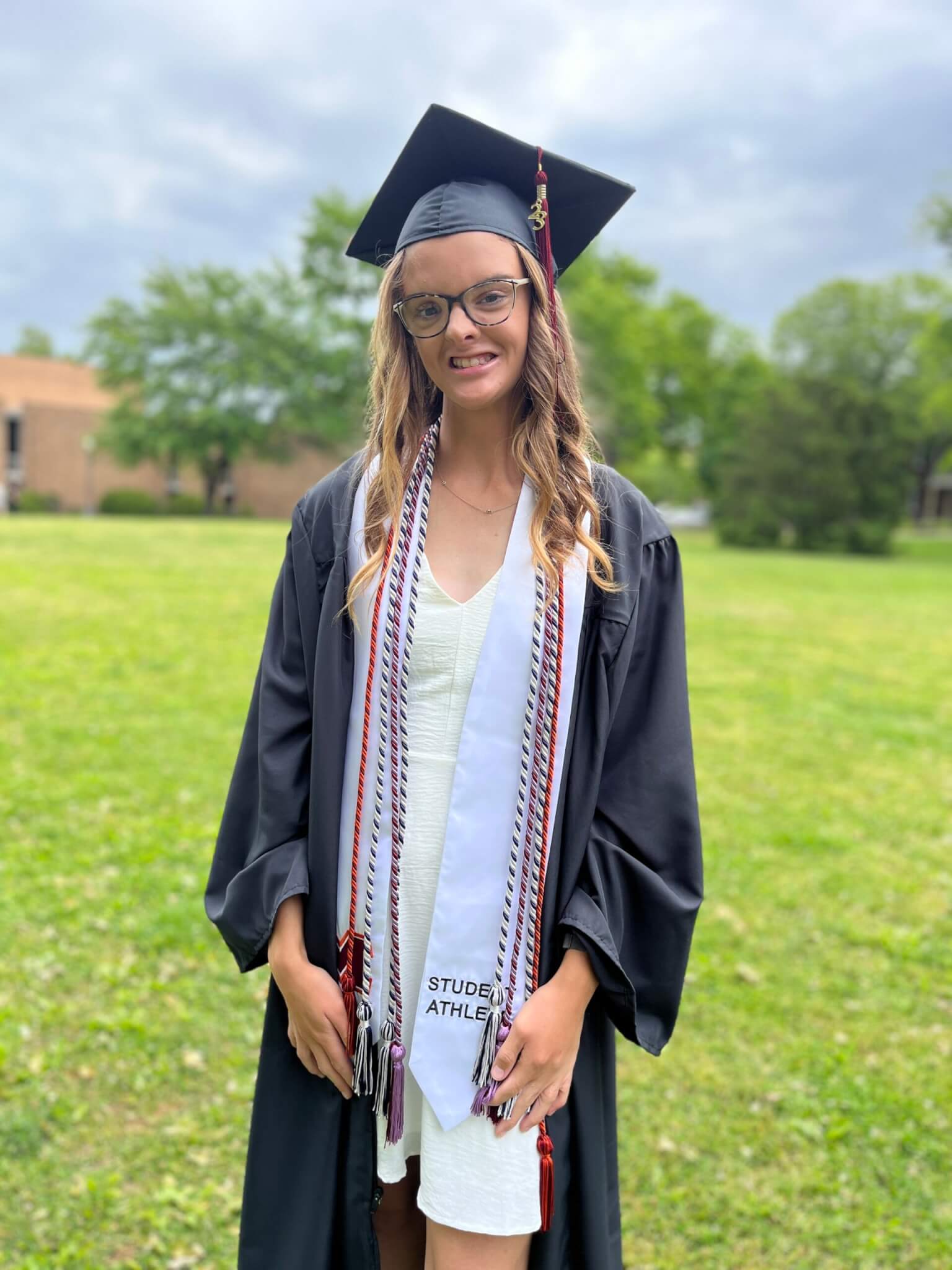 Maddie Cunningham in graduation robes standing on the lawn outside of Anderson Hall on Maryville College's campus