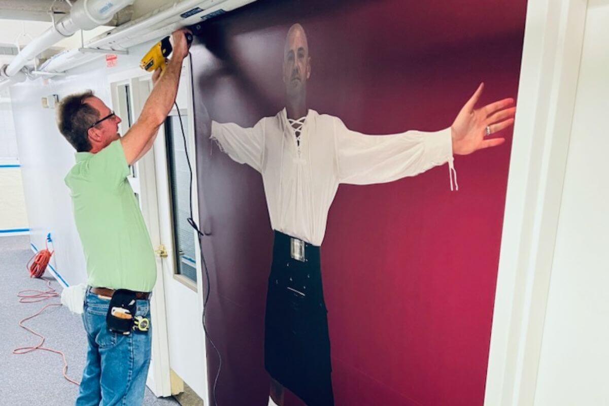 Photo of a worker from the MC Facilities Operations team working on a mural of Noah Bowman