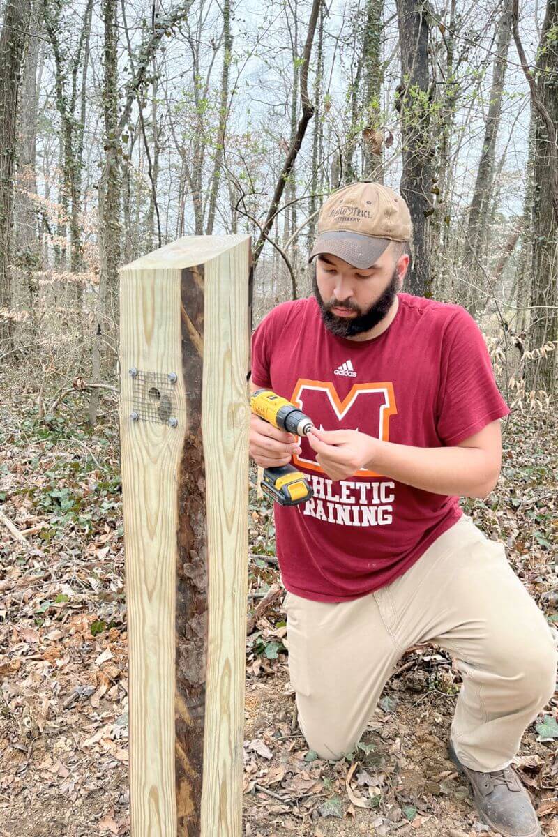 Photo of Trevor Gaines-Perry drilling holes in a 6-by-6 post