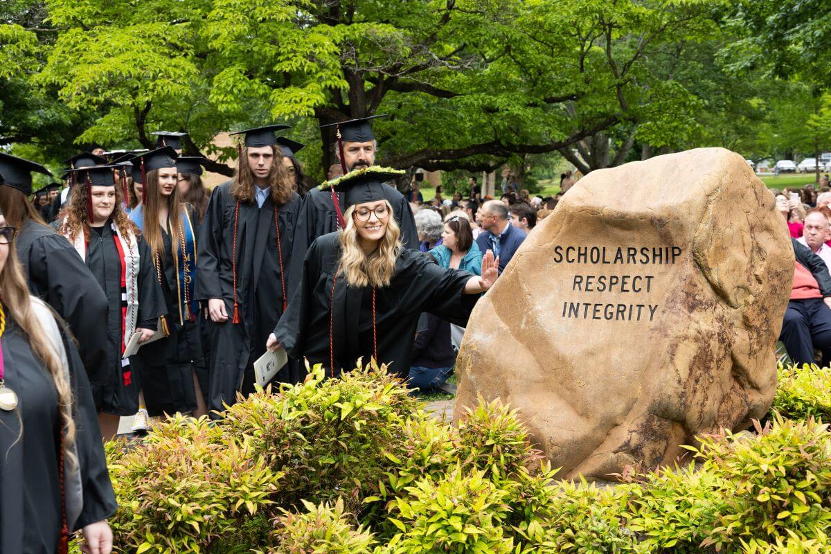 Photo of MC senior touching the Covenant Stone at Commencement 2023