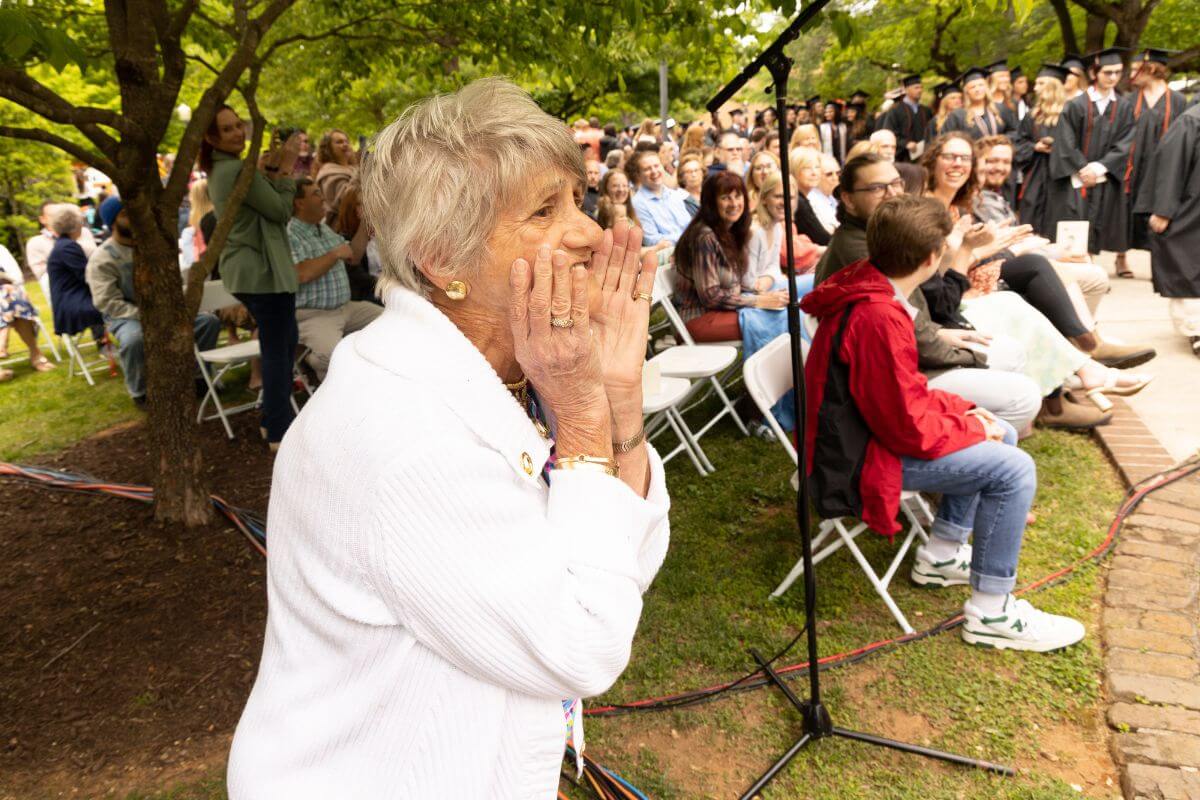 Photo of excited elderly woman yelling kudos at a graduate