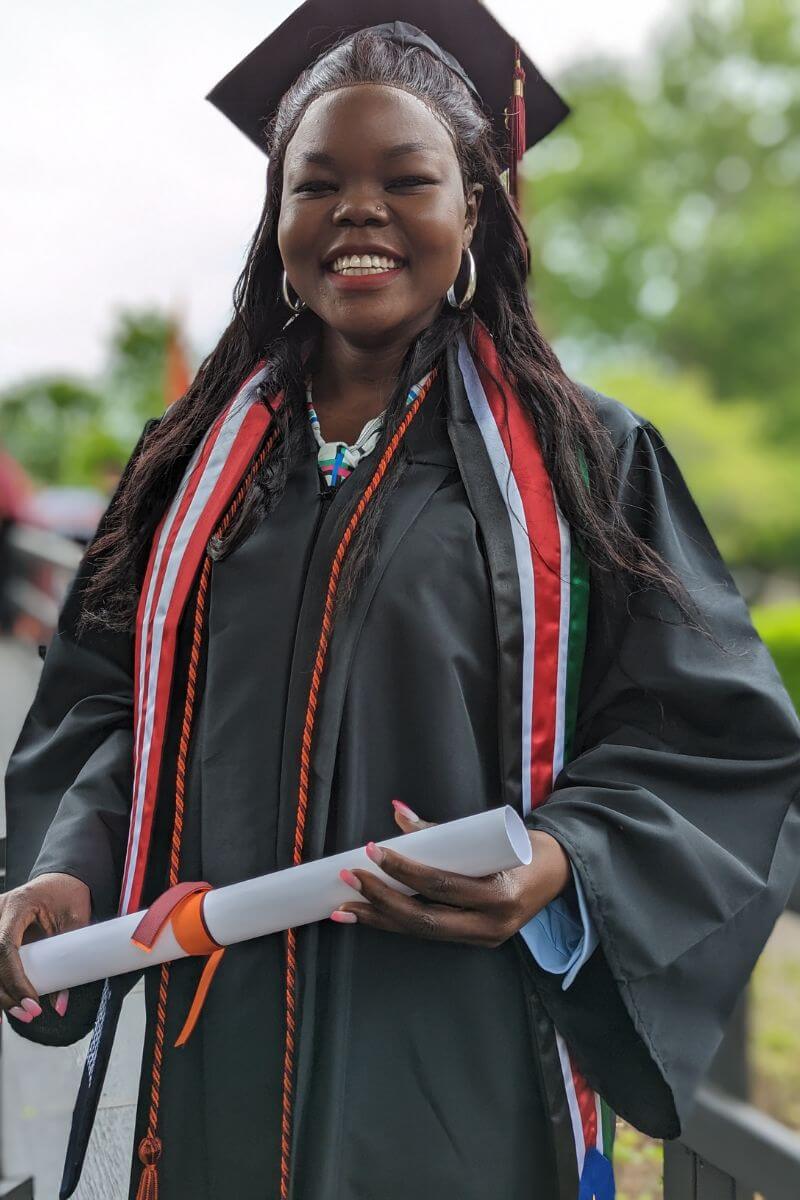 Photo of Betty Asha Adullyi smiling and holding her diploma