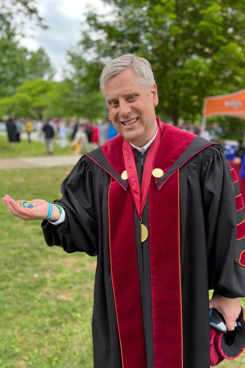 Photo of a smiling Dr. Coker holding a palm full of marbles after Commencement 2023