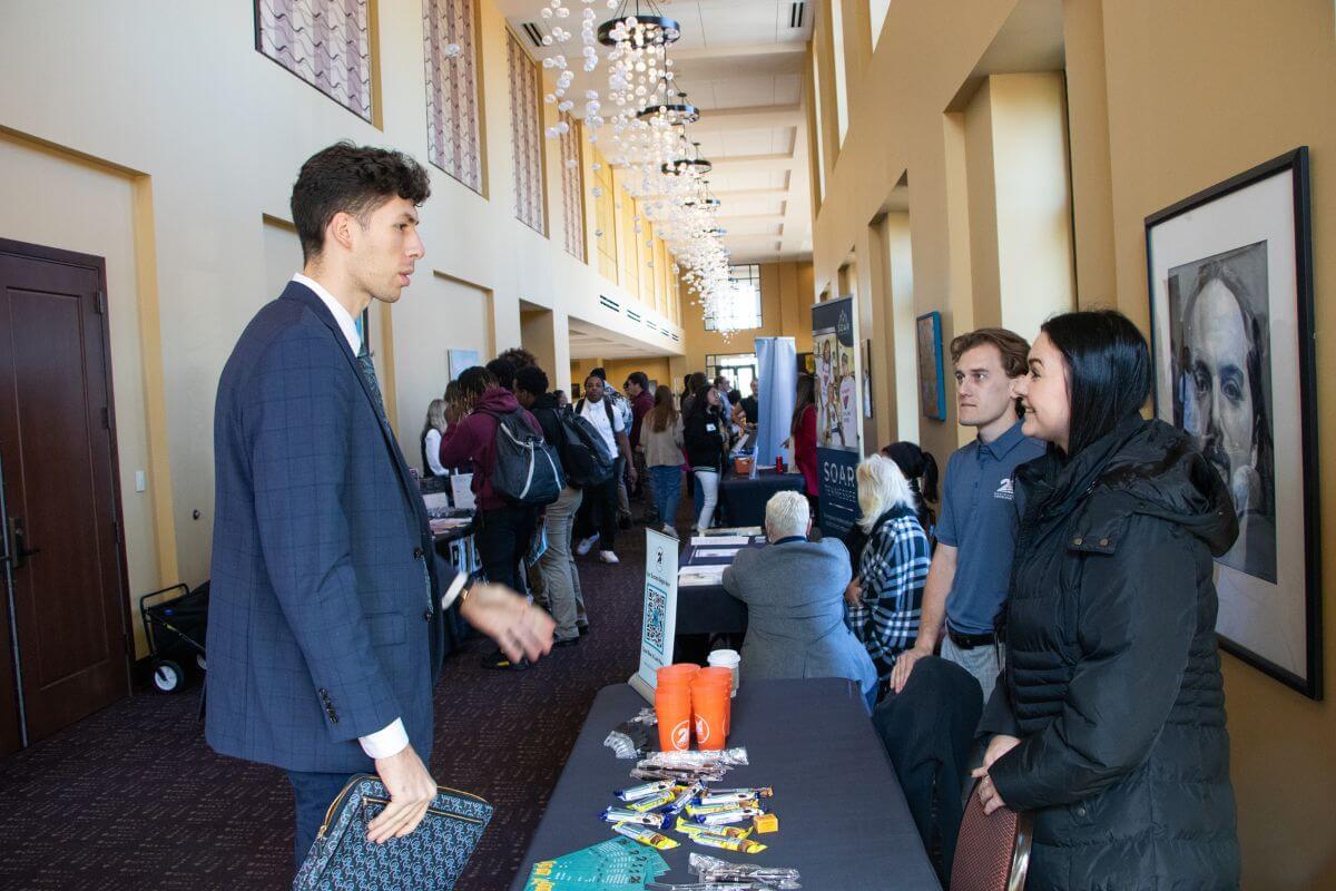 Photo of a guy in a suit and tie talking with vendor at the MC Career Fair