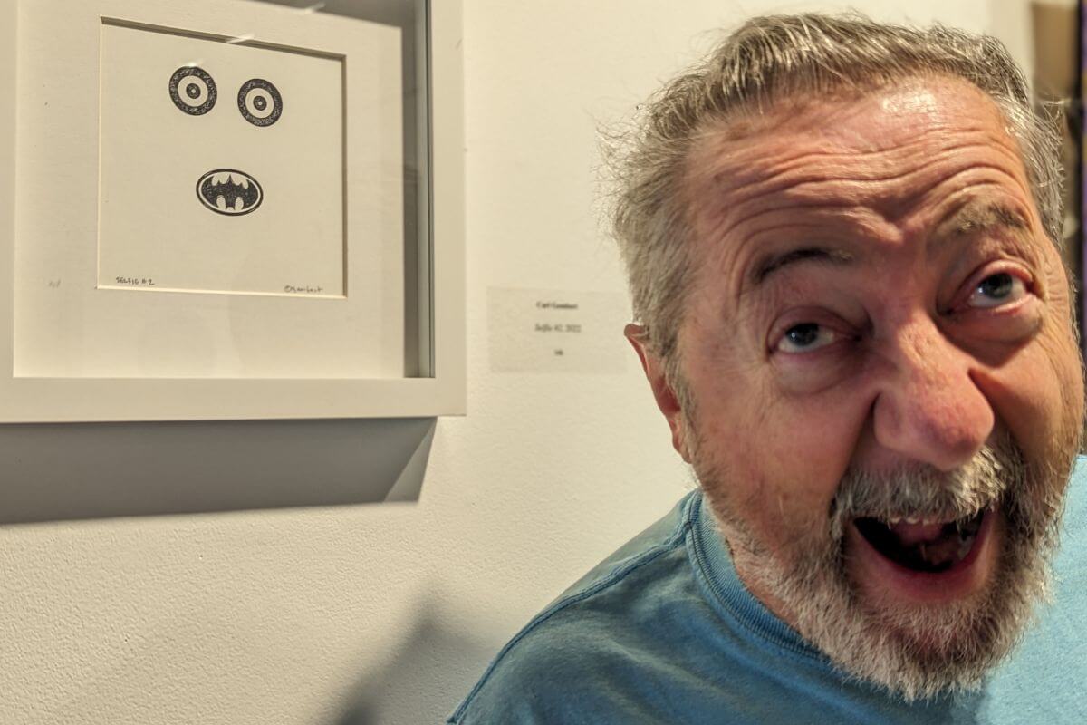 Photo of Dr. Carl Gombert making a face beside one of his pieces of art