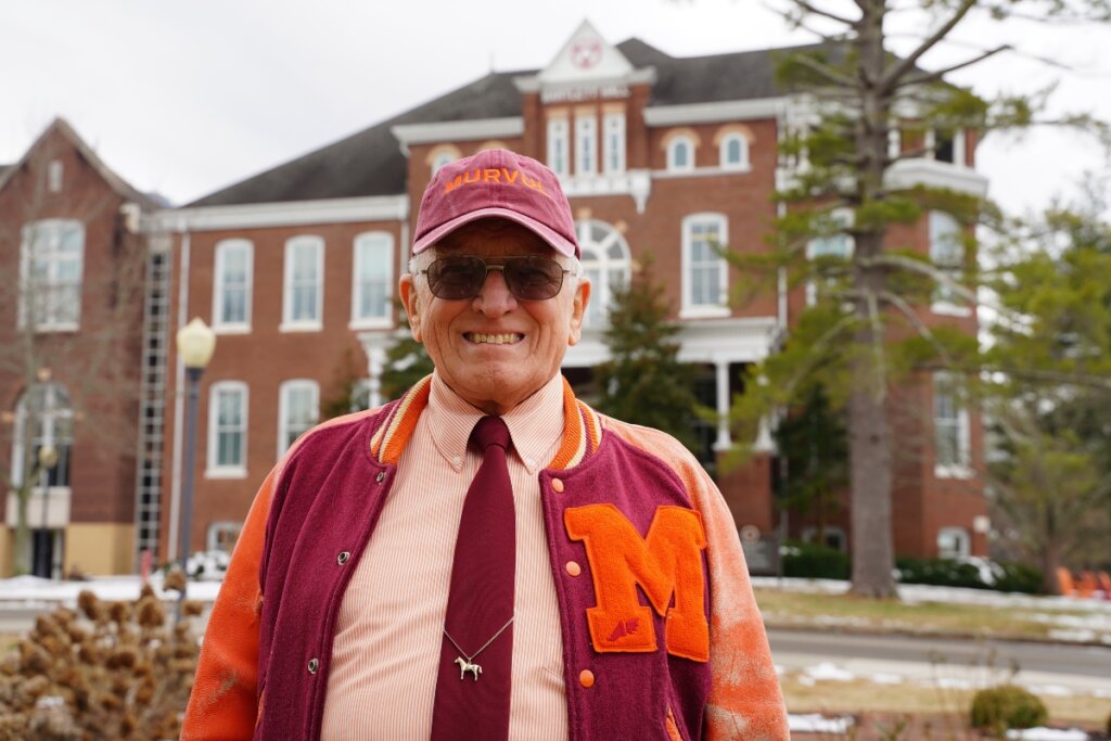 Photo of Hugh McCampbell '66, wearing a hat and smiling in front of Bartlett Hall