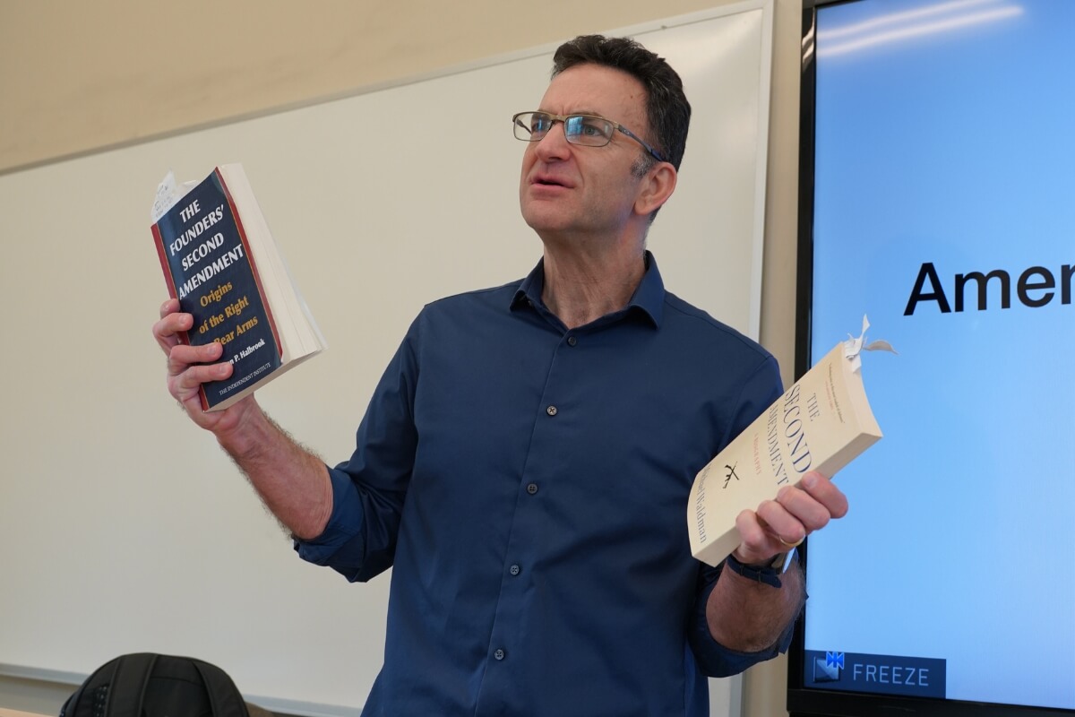 Photo of Dr. Doug Sofer holding up two textbooks for his Maryville College history of firearms course