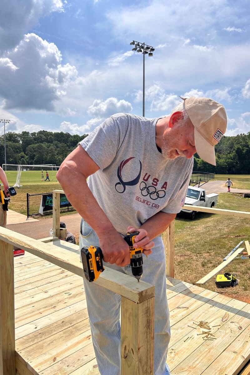 Photo of Bob Macy '70 driving screws into a deck railing