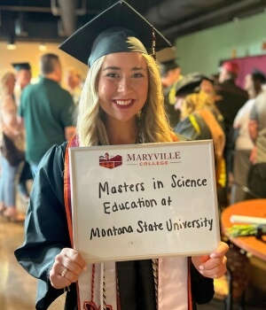 Photo of Ava Whitemire '24 holding a dry erase board in a crowded lobby