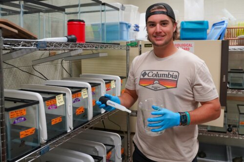 Photo of Christian Carlton '24 in a laboratory filled with fish tanks