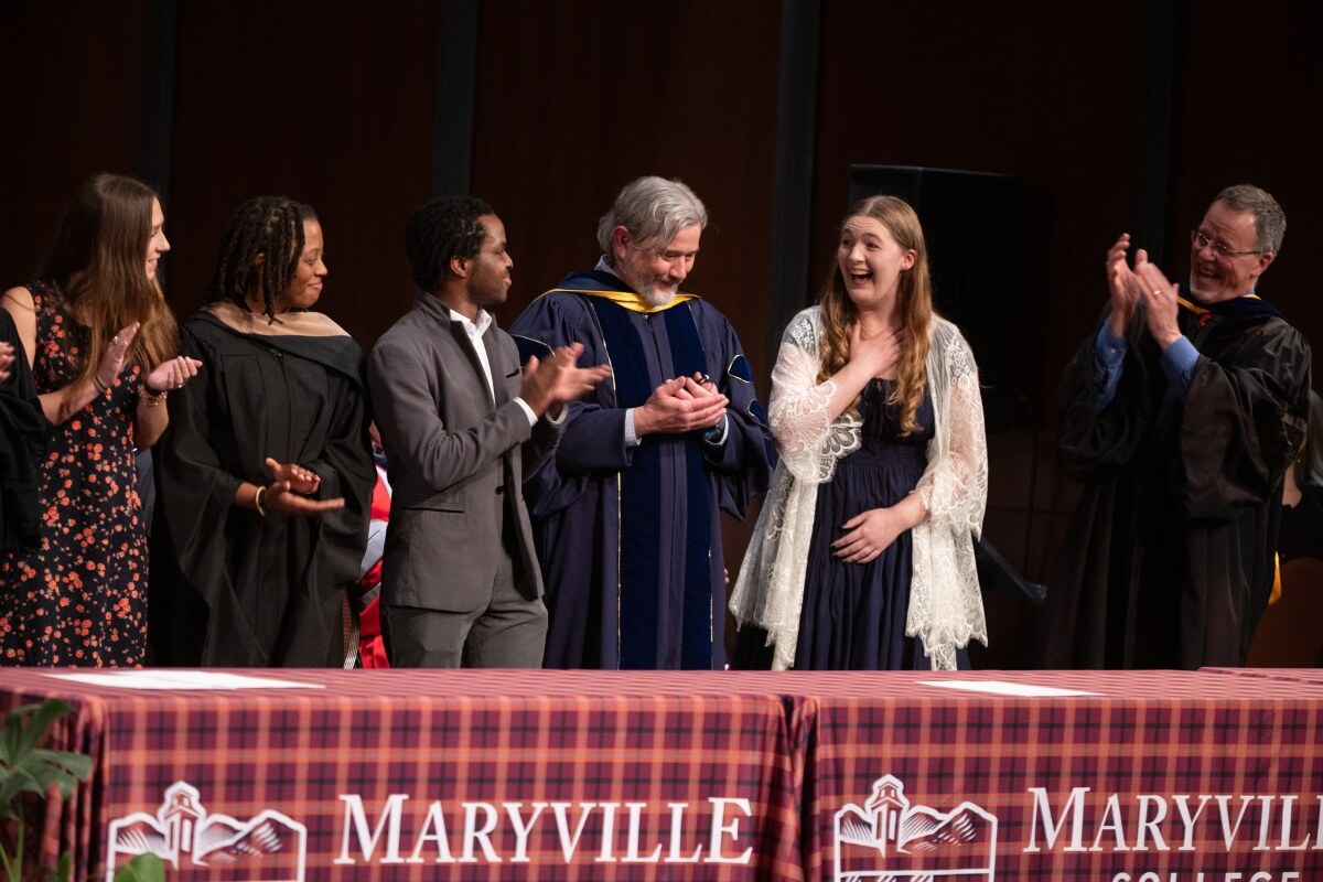 Photo of a surprised young lady surrounded by clapping peers