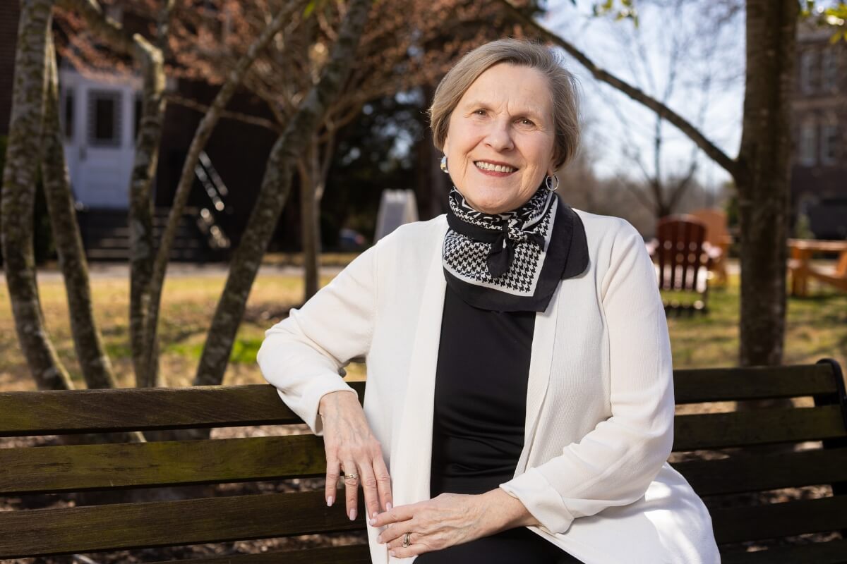 Photo of an elderly woman sitting on a bench and smiling at the camera