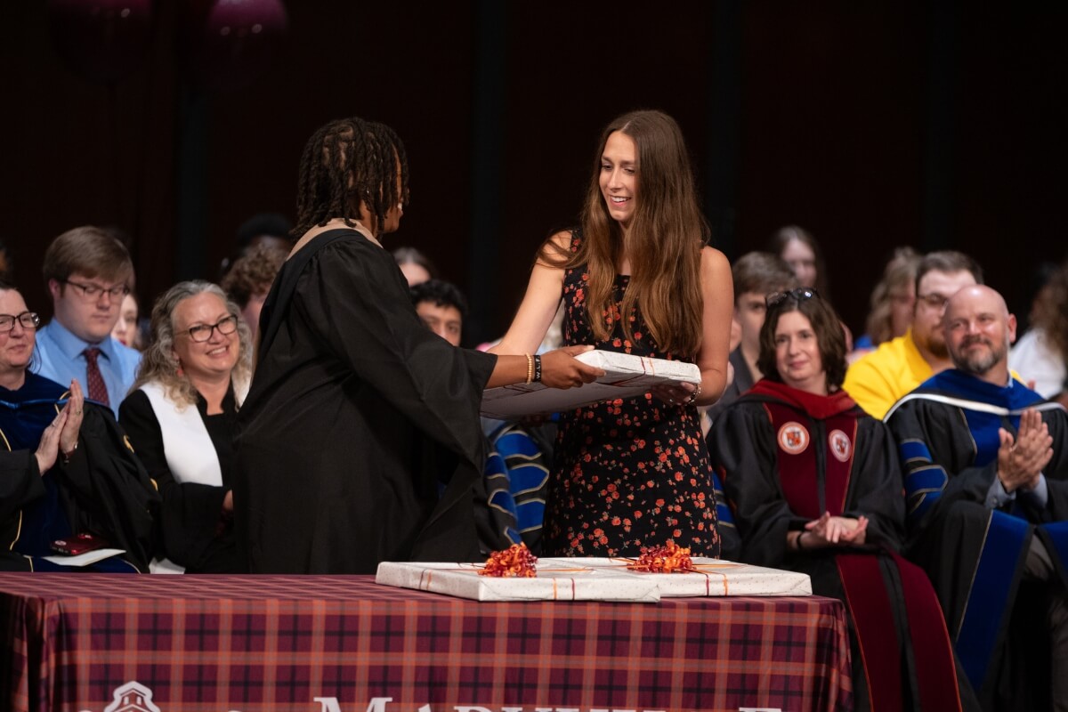 Photo of a Black Woman handing a fancily wrapped package to a tall girl