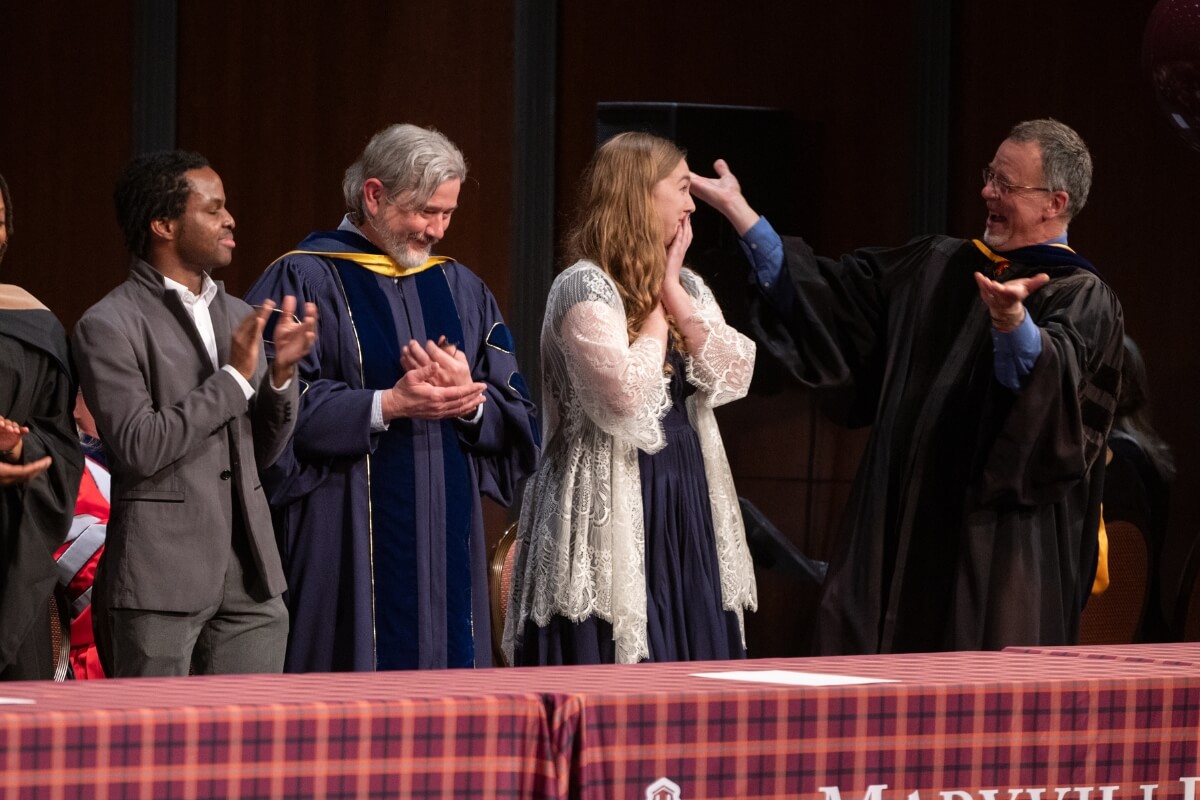 Photo of the 2025 Outstanding Senior Award winner reacting to her name being called while a professor gestures at her