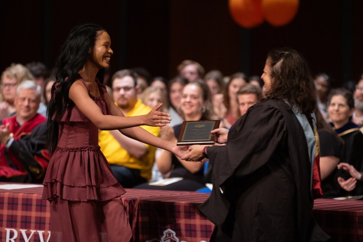Photo of a Black girl smiling and receiving a certificate from a Maryville College staff member
