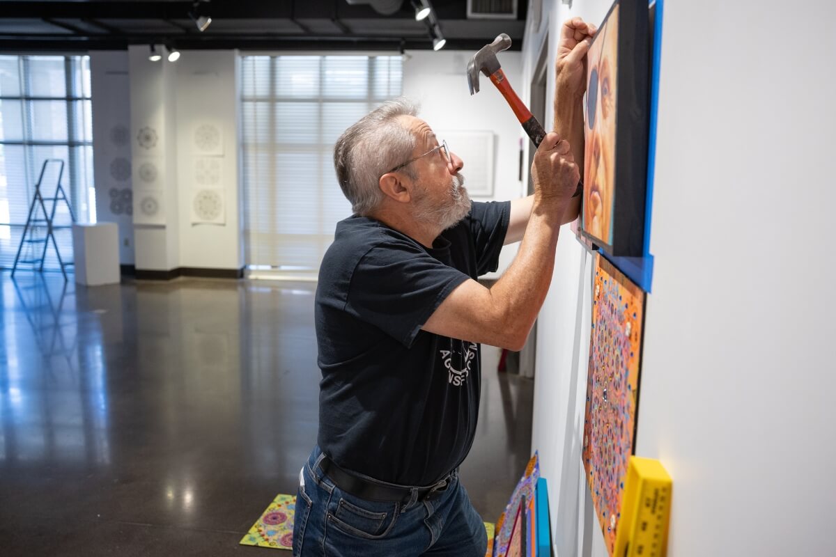 Photo of Dr. Carl Gombert adjusting work in his upcoming art exhibit at the Clayton Center.
