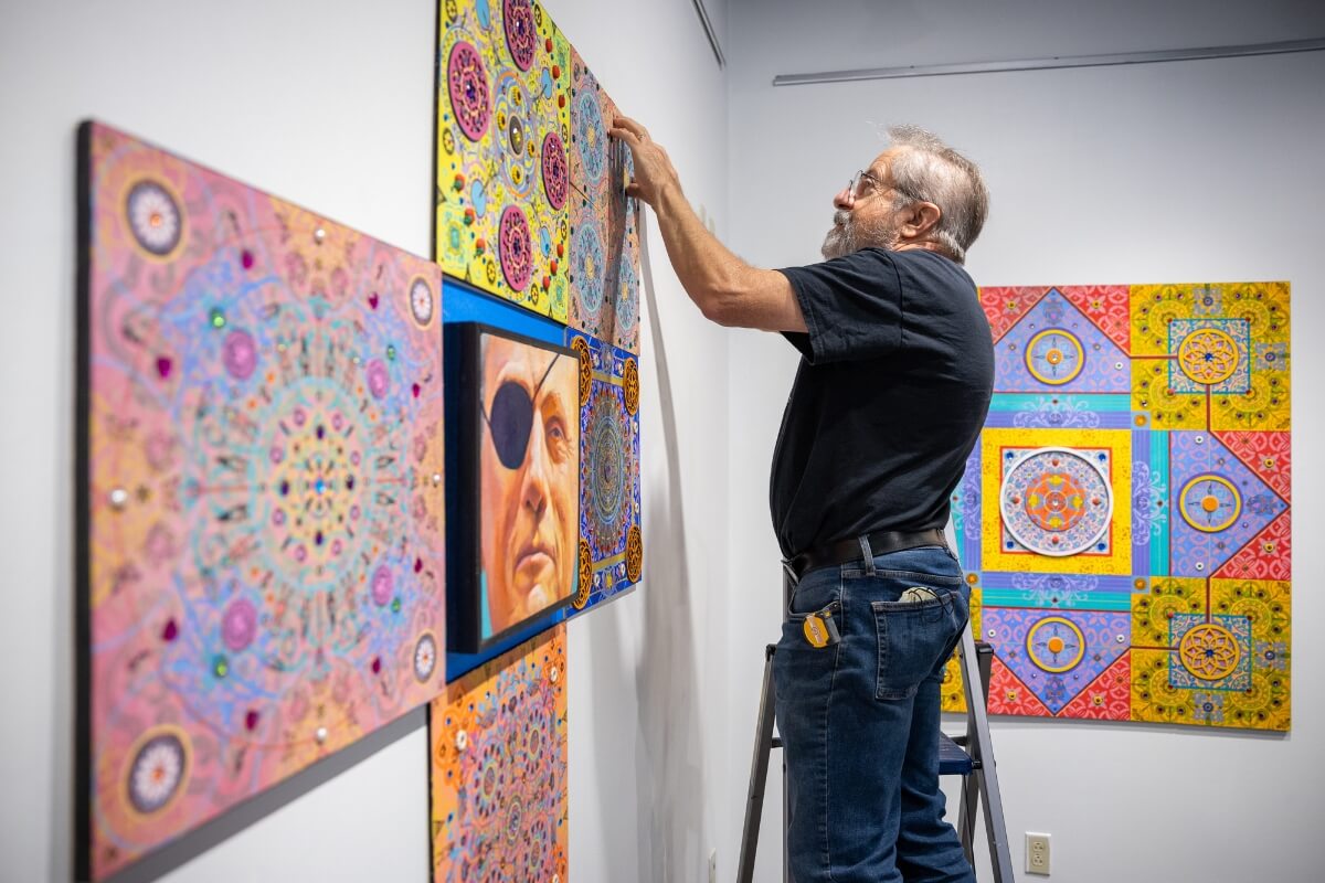 Photo of Carl Gombert hanging his artwork on the wall of an art gallery