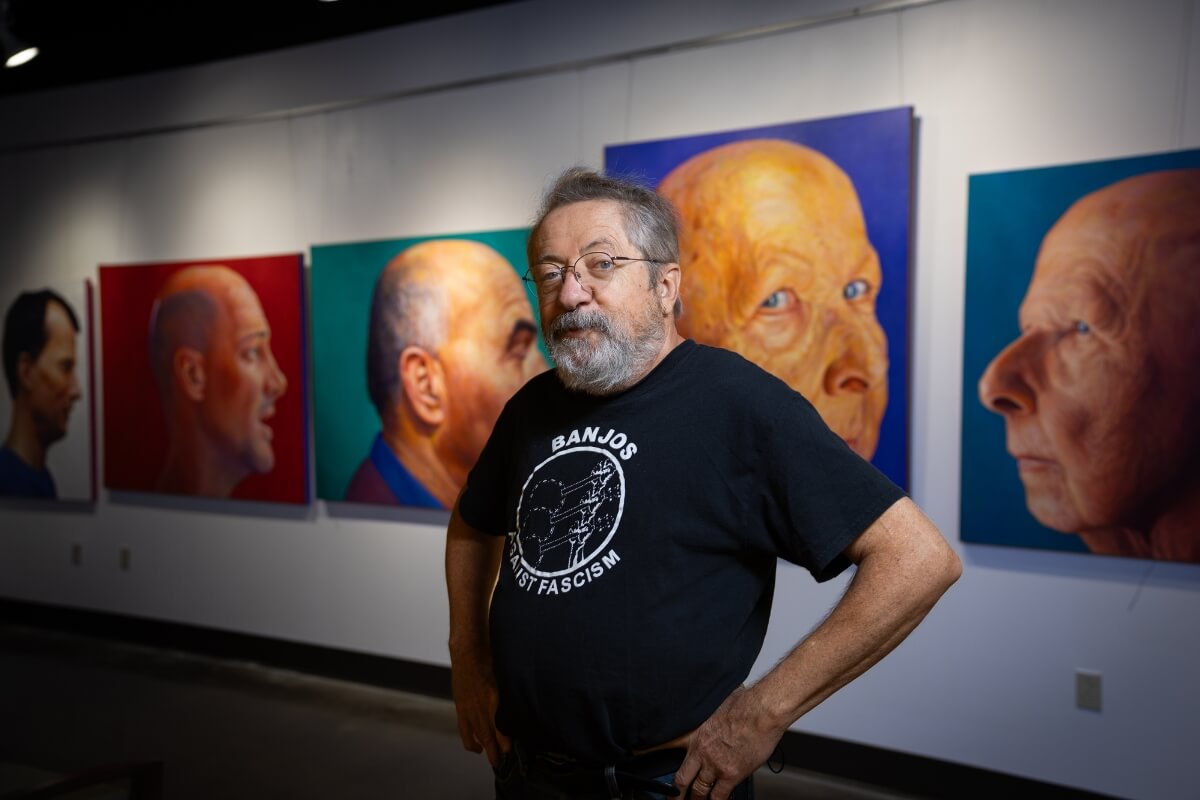 Photo of Dr. Carl Gombert standing before his latest art exhibit