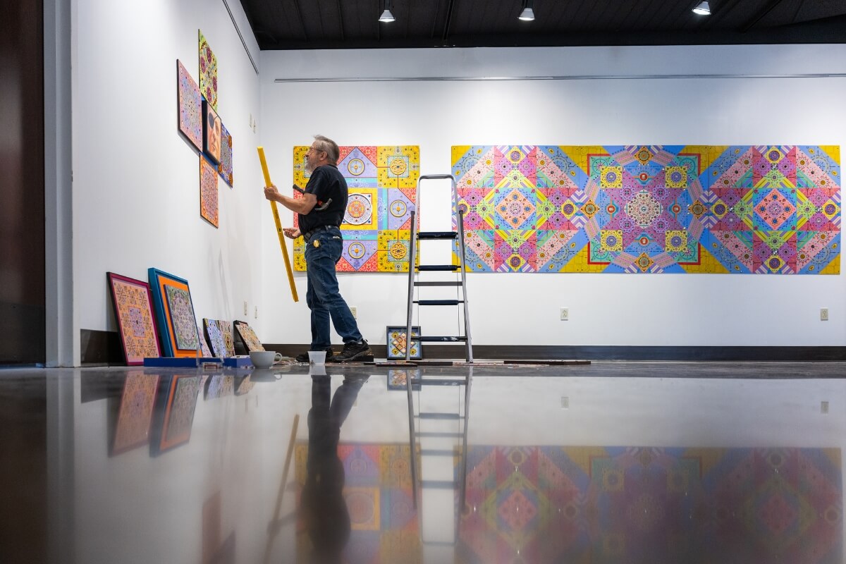 Photo of Dr. Carl Gombert approaching a wall containing his art exhibit works