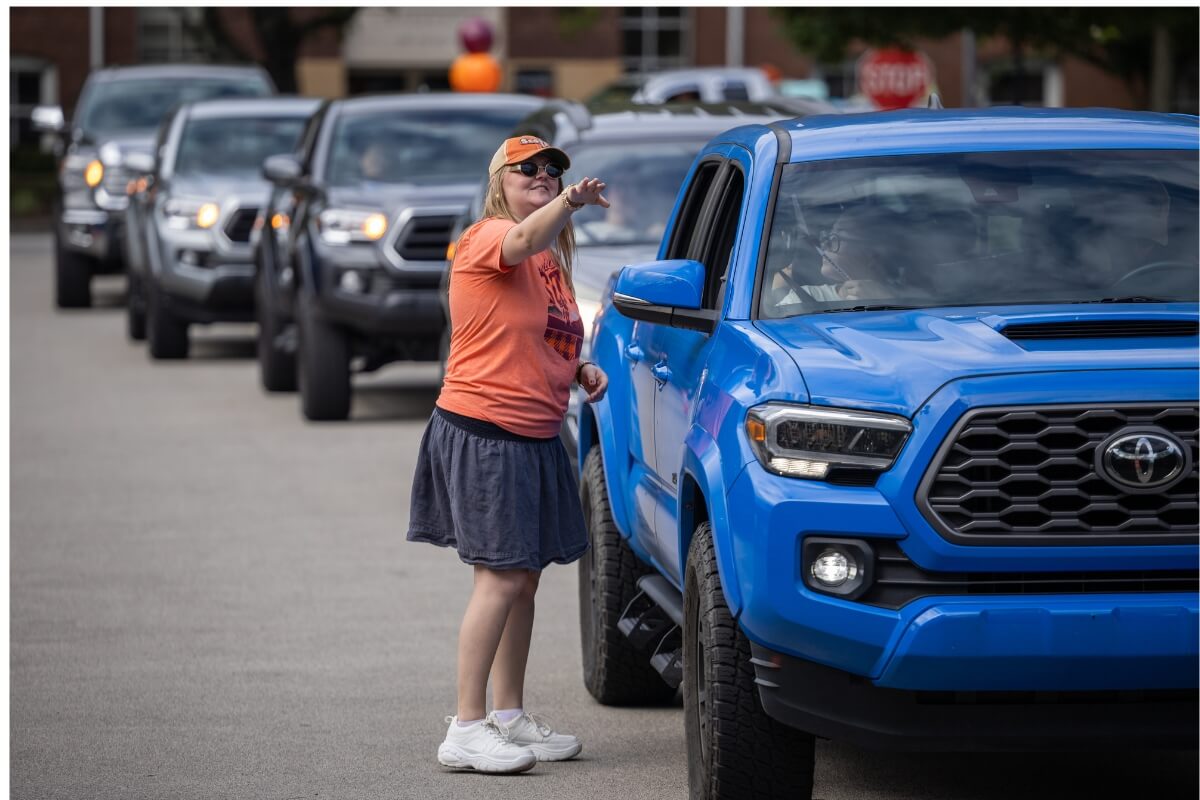 Photo of a woman standing beside a line of cars and pointing