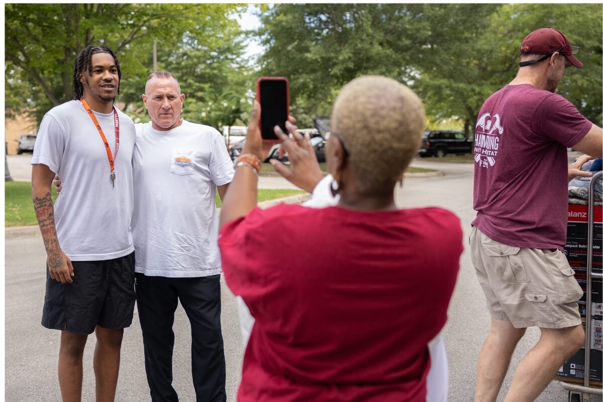 Photo of a mother taking a photo of her son and his father outside a Maryville College dorm