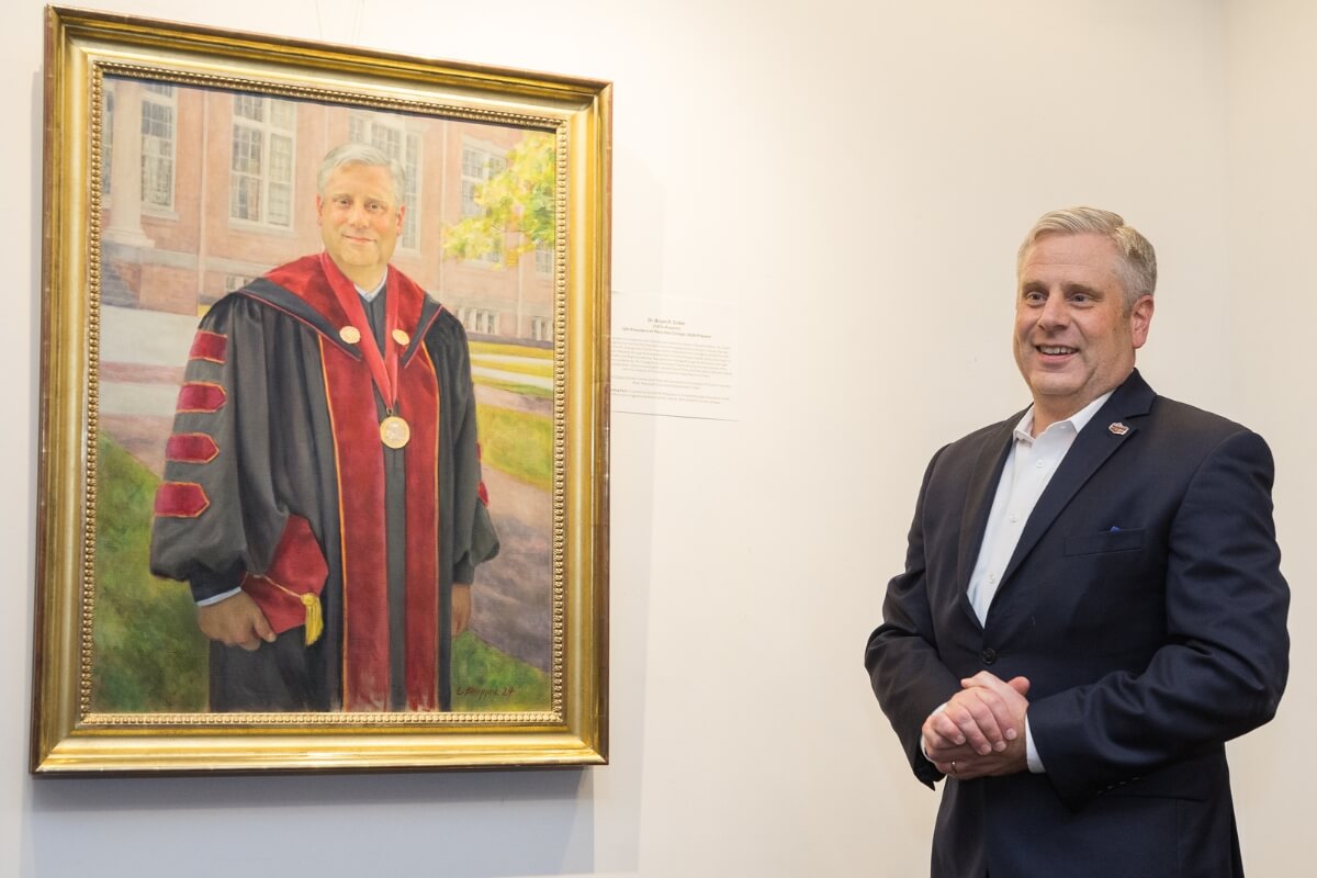 Photo of Bryan Coker smiling beside his presidential portrait
