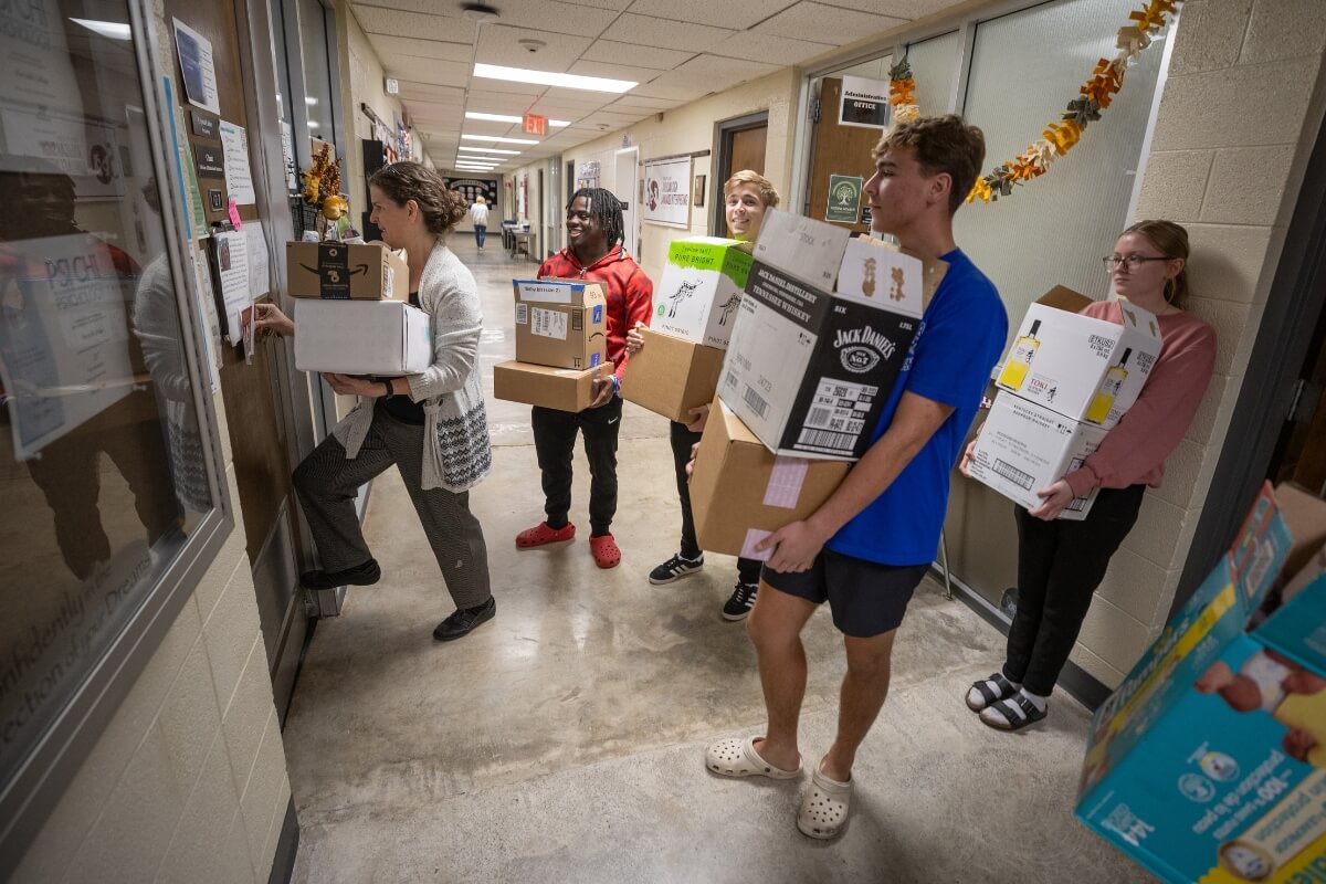 Photo of students standing in a hallway with arms full of boxes
