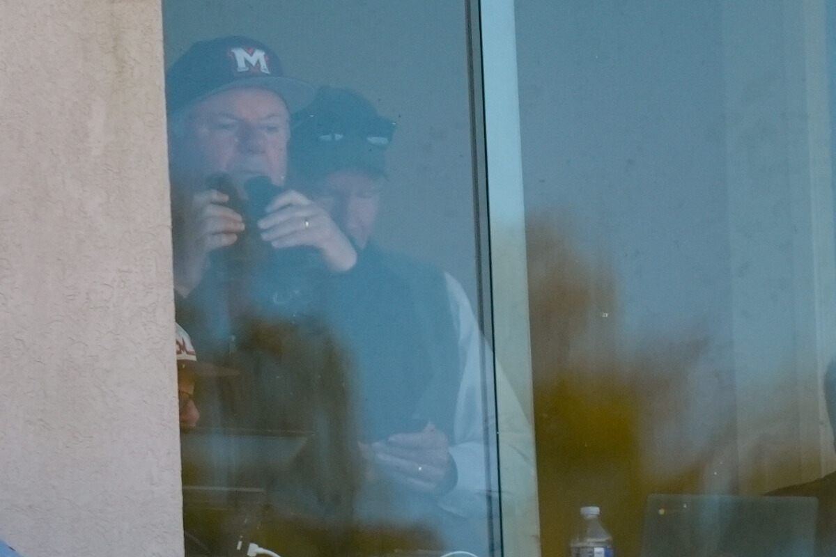 Photo of John Painter behind the press box glass with a pair of binoculars