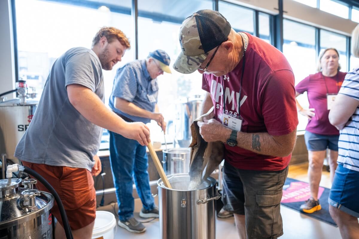 Photo of two alumni pouring grains into a fermentation barrel at the MC Downtown Center