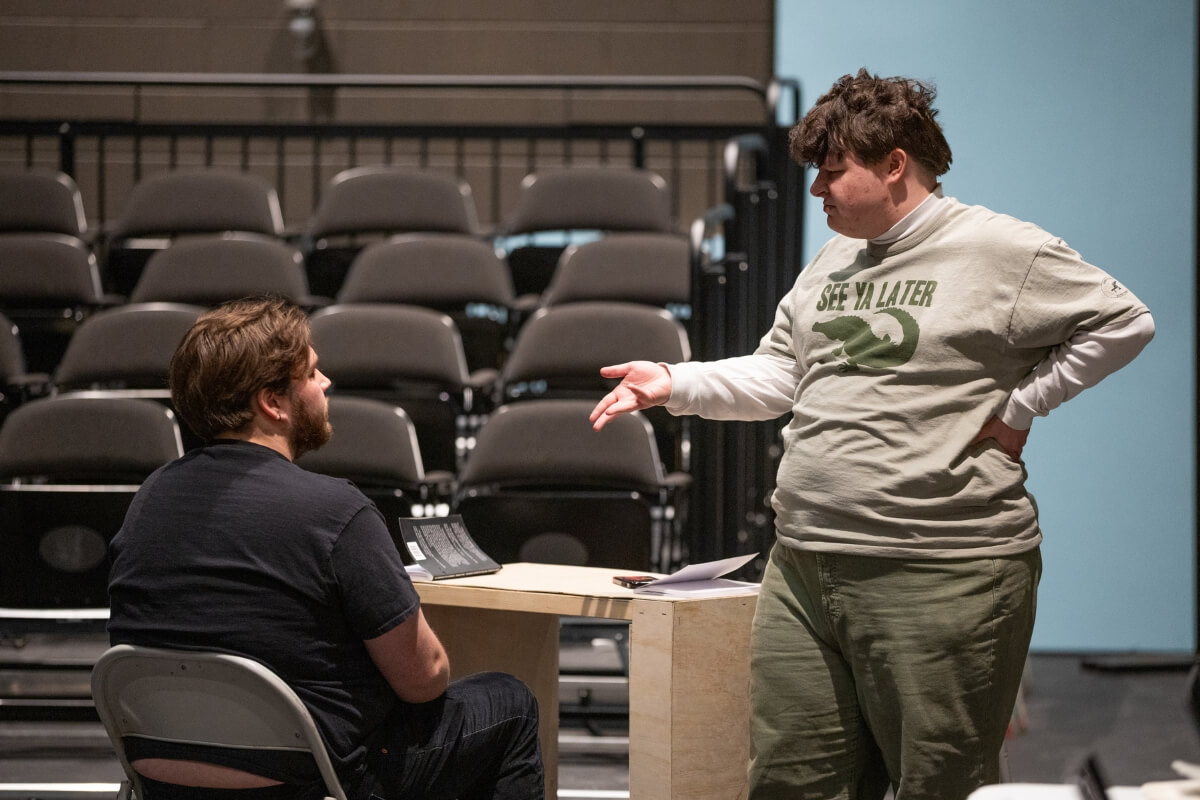 Photo of two Maryville College students, one seated and one standing, rehearsing a scene from "Angels in America"