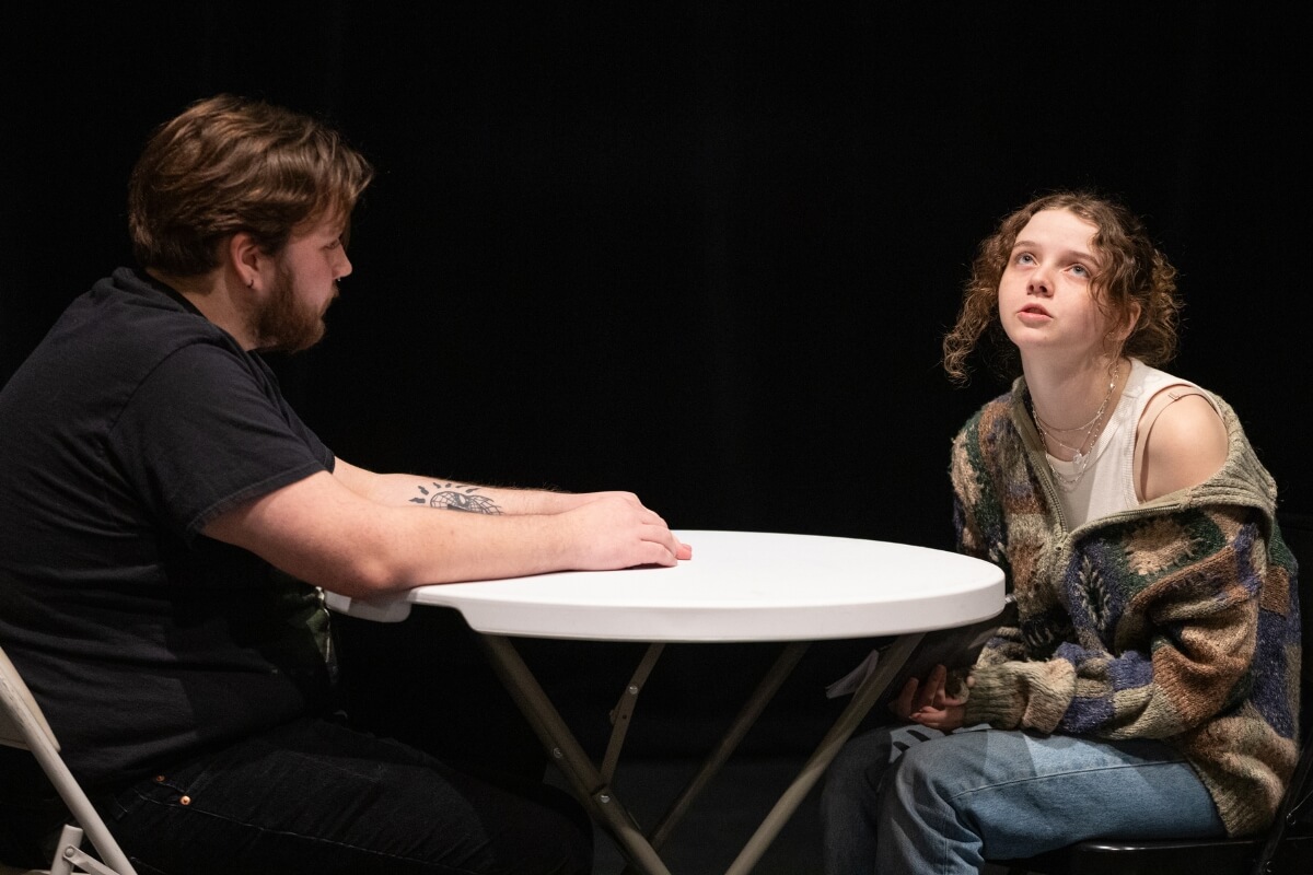 Photo of two MC students acting out a scene while seated at a table