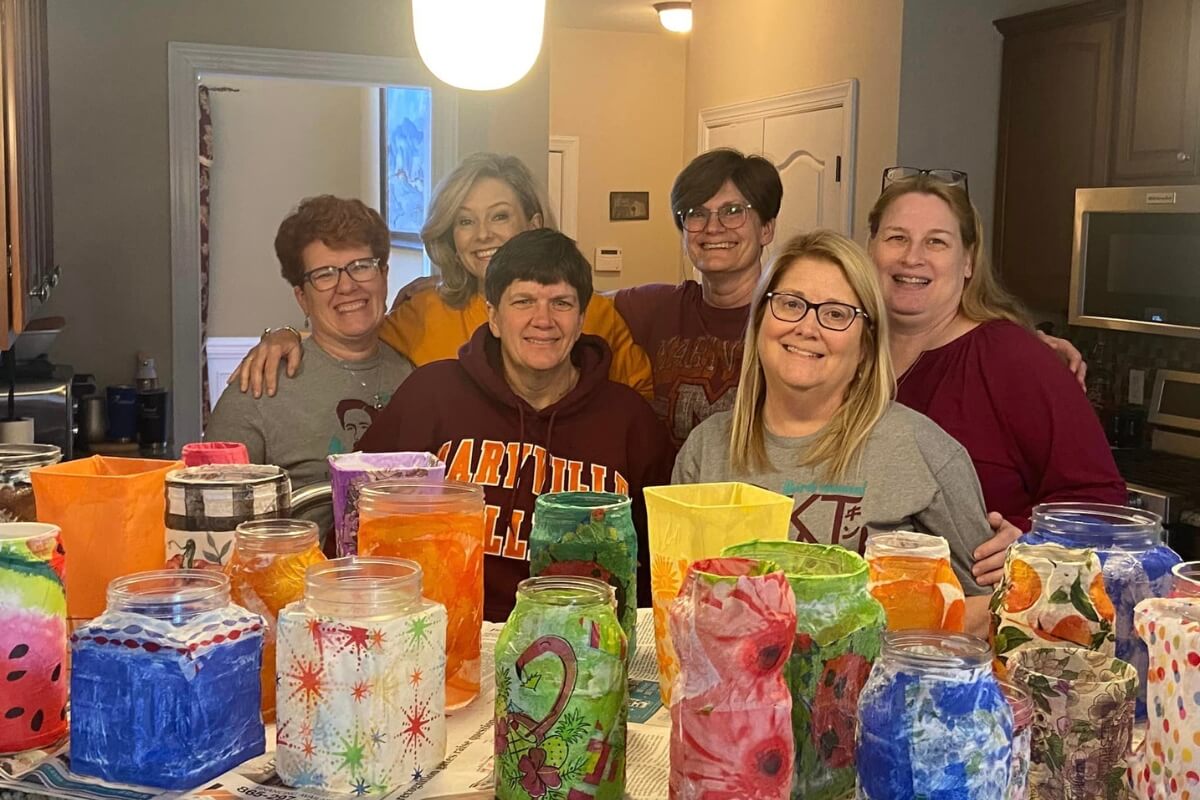 Photo of six smiling women in front of a table of decorative vases