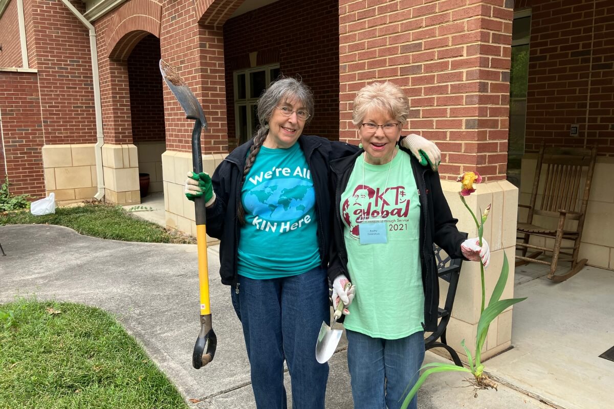 Photo of two smiling women holding gardening implements