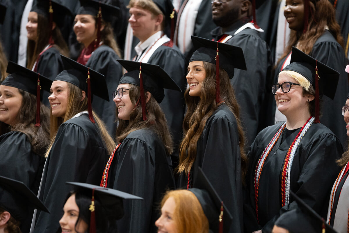 Photo of a group of smiling graduates standing in the auditorium, looking at the stage