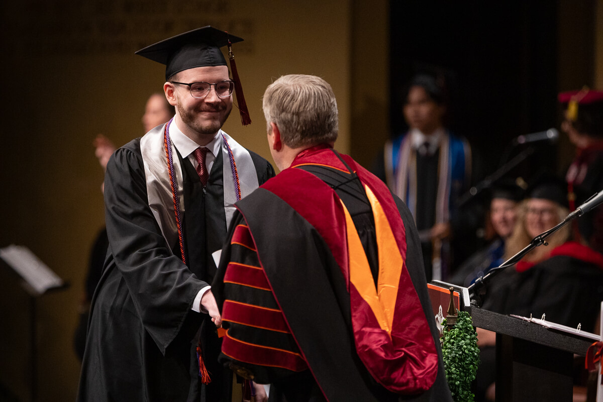 Photo of Dr. Bryan Coker, back to the camera, handing a diploma to a smiling Maryville College Commencement 2025 senior
