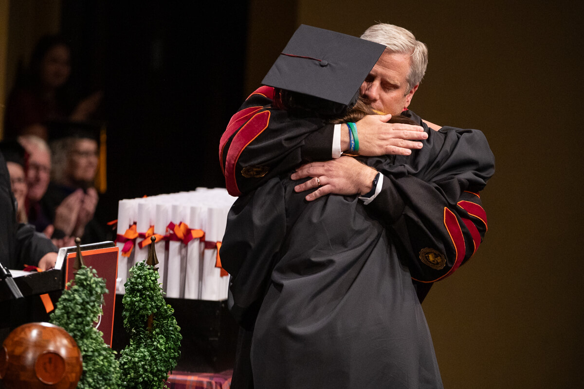 Photo of Dr. Bryan Coker hugging a student on stage during Commencement