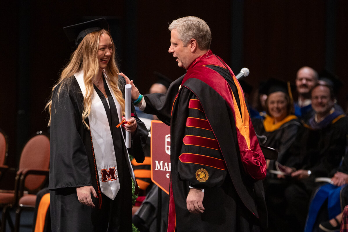 Photo of a smiling girl in cap and gown receiving a diploma from the Maryville College president during Maryville College Commencement 2025