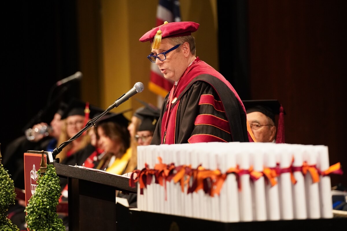 Photo of Dr. Bryan Coker at a podium with diplomas in the foreground