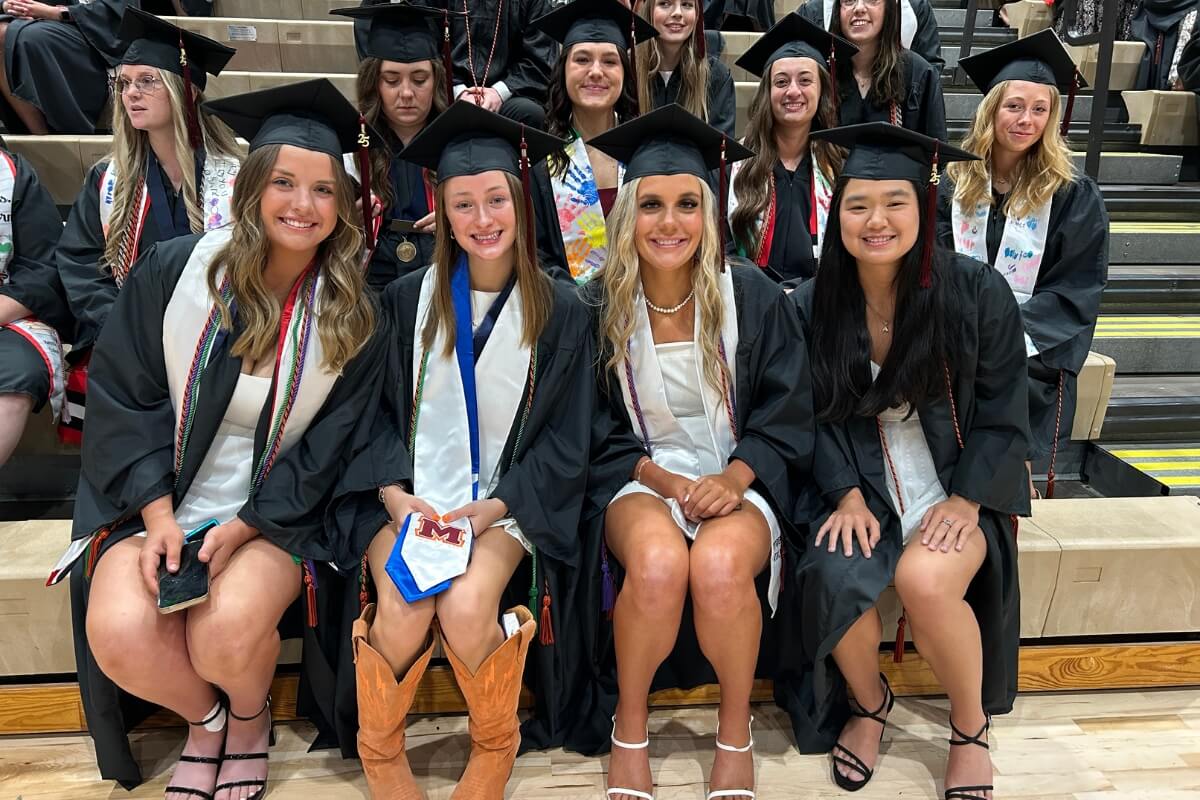Photo of several female graduates of Maryville College sitting on bleachers in their caps and gowns